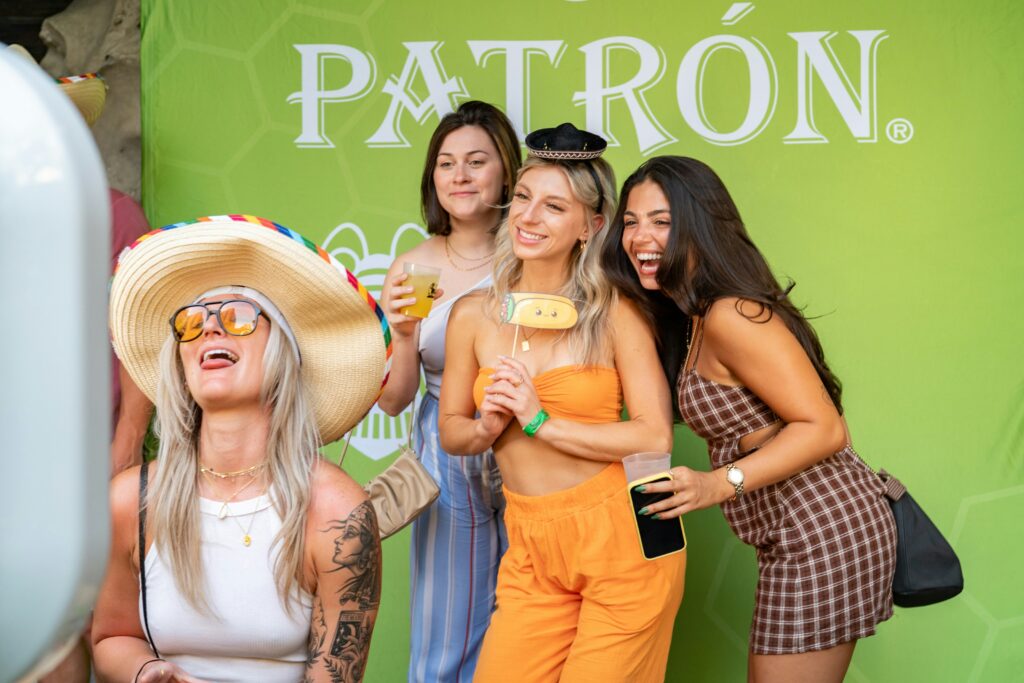 Group of guests using a photo booth with fun props in front of a branded event backdrop